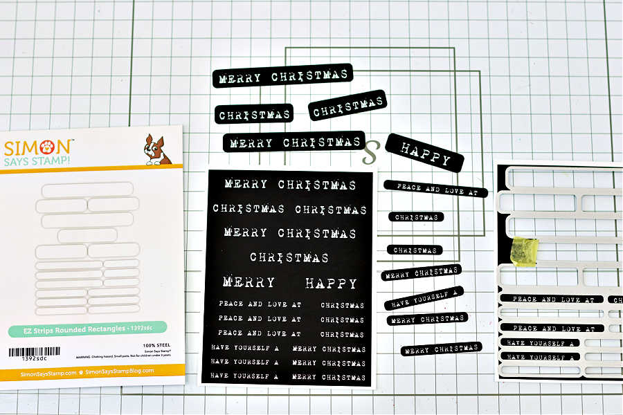 Die-cutting Simon Says Stamp EZ Strips Reverse Vintage Christmas preprinted sentiment sheets using the EZ Strips Rounded Rectangles Die Set. The black-and-white sentiment panels feature phrases like “Merry Christmas,” “Have Yourself,” and “Peace and Love at Christmas.” The dies and cut-out sentiments are displayed on a gridded work surface, ready for card assembly. Designed by Sandi MacIver.