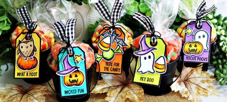 Five black metal pails filled with colorful Halloween candies are topped with clear treat bags tied with black-and-white gingham ribbon. Each pail features a bright handmade tag created with the Tim Holtz Tiny Frights Stamp Set, showcasing cute Halloween images—a ghost, owl, pumpkin, bat, and candy—colored in vibrant shades of orange, teal, purple, and lime green. The tags display playful sentiments like “What a Hoot,” “Wicked Fun,” “Here for the Candy,” “Hey Boo,” and “Hocus Pocus,” making them perfect for festive Halloween gift giving.