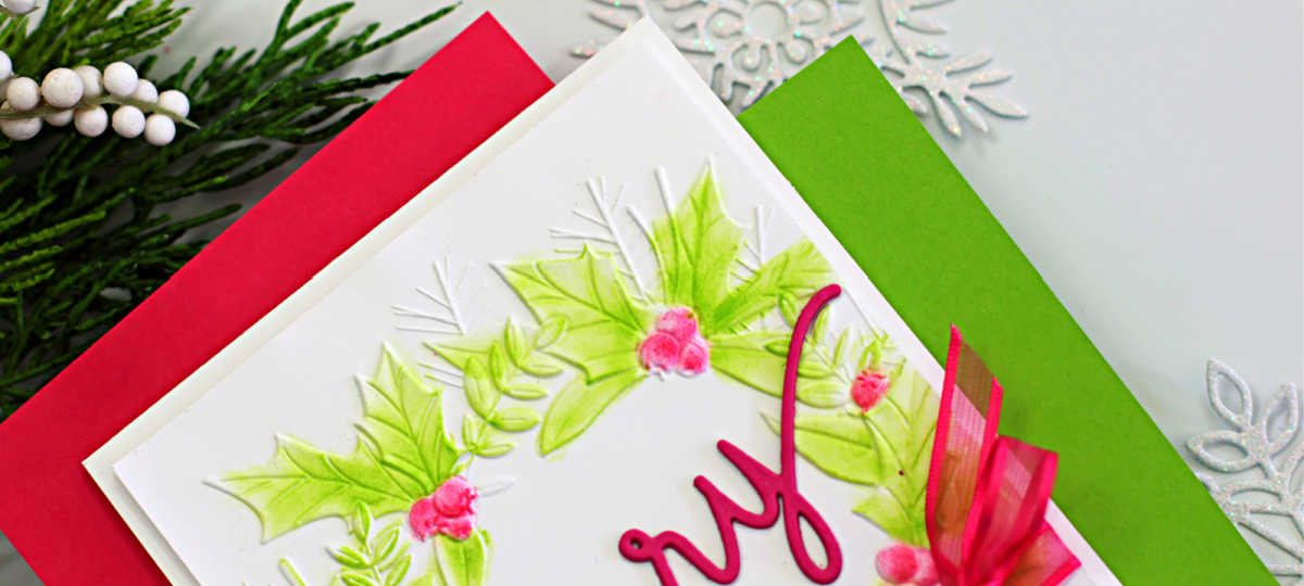 Handmade Christmas card featuring the Simon Says Stamp Festive Wreath Embossing Folder, ink-blended with soft green and pink hues to highlight the raised holly leaves and berries. The card is finished with a bold pink “merry” die-cut sentiment from the Holiday Duo Die Set and accented with a sheer pink ribbon bow tied around the panel. Layered on red and green cardstock for a festive, elegant presentation.