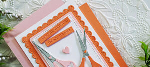 Handmade card created with the Spellbinders Sharon’s Scissors Die Set in honor of Sharon Klima for World Fussy Cutting Day. The design features two pairs of heart-handled scissors in soft pink and coral tones arranged on layered scalloped and stitched rectangle panels. A small heart embellishment and the sentiment “You’re Always in My Heart” complete the layout, symbolizing creativity, friendship, and heart health awareness.