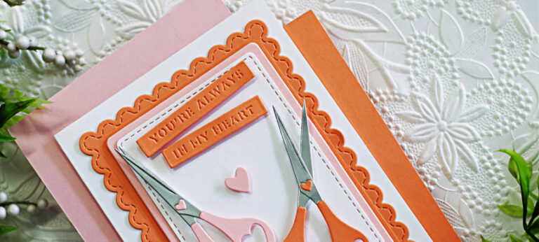 Handmade card created with the Spellbinders Sharon’s Scissors Die Set in honor of Sharon Klima for World Fussy Cutting Day. The design features two pairs of heart-handled scissors in soft pink and coral tones arranged on layered scalloped and stitched rectangle panels. A small heart embellishment and the sentiment “You’re Always in My Heart” complete the layout, symbolizing creativity, friendship, and heart health awareness.