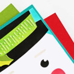 Handmade Frosty snowman Christmas card created with the Spellbinders Stencil of the Month Club ‘Frosty Wishes.’ Features a cheerful snowman face with a carrot nose, rosy cheeks, and a green top hat accented with holly, layered on a bright turquoise card base for a fun and festive holiday design.