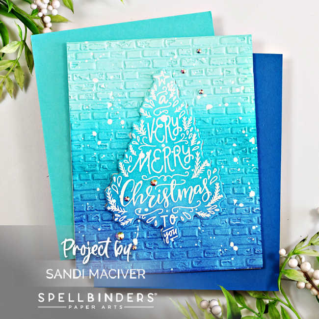 Handmade holiday card created by Sandi MacIver using the Spellbinders To You and Yours Clear Stamp and Die of the Month and the 3D Embossing Folder of the Month. The design features a blue ombré ink-blended background embossed with a brick pattern, overlaid with a white embossed Christmas tree-shaped sentiment that reads “A Very Merry Christmas to You.” The card is accented with white paint splatters and small clear gems for sparkle, layered over teal and navy blue cardstock panels.