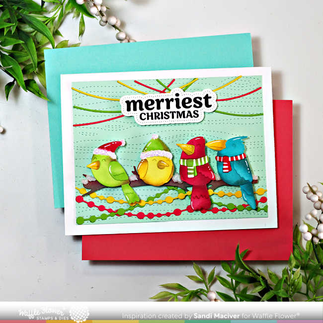 Handmade Christmas card created with the Waffle Flower Birdie Friends dies and coordinating stencils. The design features four colorful, ink-blended birds—green, yellow, red, and blue—each wearing festive winter hats and scarves, perched on a branch against a pale mint background embossed with the Wood Grain Texture die. Strands of stitched Christmas lights arch playfully overhead, and the bold sentiment “Merriest Christmas” from the Warm Wishes stamp and matching piercing die set is centered above the birds. The card is displayed atop red and aqua cardstock with holiday greenery accents.