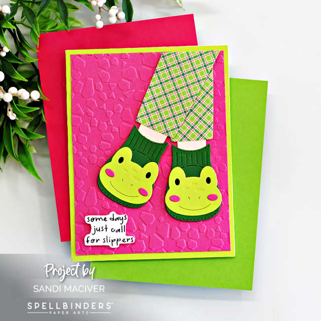 Handmade frog slipper card created with the Spellbinders Cozy Toes Friends Die Set and embossed with the Faceted Petals Embossing Folder. The card features cheerful green frog slippers paired with plaid pink-and-green pajama pants layered over a bright pink embossed background and a lime green card base. A playful sentiment strip reads “some days just call for slippers.” Designed by Sandi MacIver for Spellbinders Paper Arts.