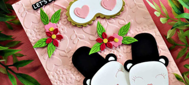 Handmade card featuring two adorable panda bear slippers nestled together on a blush pink background embossed with the Sweet Stems Embossing Folder from the Spellbinders December Club kits. Die-cut flowers and leaves decorate the card, with a coordinating sleep mask above the slippers and a black-and-white sentiment that reads “Let’s do nothing together.” Card created using the Spellbinders Deluxe Caboodle Bonus Gift of the Month.