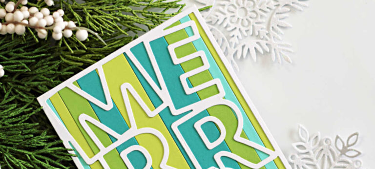 Handmade Christmas card featuring a bold “MERRY” cover die cut from white cardstock and backed with vertical strips of lime green and teal. A cute stamped snowman wearing a green-and-teal hat and scarf is sledding across the bottom right corner. Card is displayed upright on a white snowflake stand with evergreen décor and a blue ornament in the background.