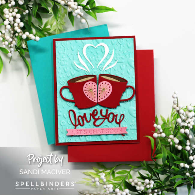 Handmade Valentine’s card featuring two red stitched coffee mugs with pink heart centers created using the Spellbinders Stitched Die of the Month “A Perfect Blend.” The mugs meet in the middle with white steam forming a heart above them. The sentiment “love you” is die-cut in red with a pink banner reading “Let’s Chat Soon.” The aqua card front is embossed with the Unlock My Heart 3D Embossing Folder and layered on red and aqua cardstock, surrounded by greenery and white berry accents.