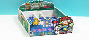 Decorated MemoryDex card holder box created with AALL & Create products for the MemoryDex Card Challenge. The box is covered in bright mixed-media collage papers with words like “Sunshine” and “Love,” and features whimsical die-cut images including a colorful girl with a flower crown, a small white dog, a sun and cloud, and a pink “Kiss” label. The box is photographed against a teal background with the sandimaciver.com watermark at the bottom.