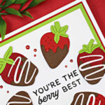 Handmade 5-inch square Valentine card featuring die-cut chocolate-covered strawberries arranged in a circle around the sentiment “You’re the berry best.” The strawberries are layered in red, brown, and green cardstock on a white panel with red and green mat layers, set against a red background.