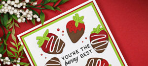 Handmade 5-inch square Valentine card featuring die-cut chocolate-covered strawberries arranged in a circle around the sentiment “You’re the berry best.” The strawberries are layered in red, brown, and green cardstock on a white panel with red and green mat layers, set against a red background.