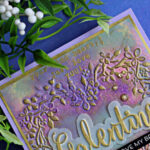 Handmade Galentine’s card featuring a heart wreath embossing folder background colored with Distress Oxide ink sprays and heat embossed in gold. The pastel purple, pink, and blue panel is layered on a lavender card base and finished with a gold-foiled “Galentine” sentiment and small gold embellishments, styled with flowers and greenery.