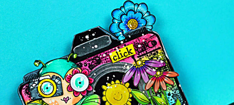 A bright, mixed-media AALL & Create MemoryDex card for Theme #1 Photography, featuring a whimsical fairy character holding a camera in front of a large rainbow-colored camera with a smiling sun lens, layered flowers, grass, paint splatter details, and a “click” label on a teal background.