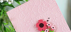 Handmade pink card featuring a soft blush ink-blended background embossed with the Spellbinders January 2026 Embossing Club “Cloud Nine” folder, layered die-cut flowers from the Small Die of the Month, and a black heat-embossed “Have a Nice Day” sentiment from the Clear Stamp and Die of the Month, finished with black gems.