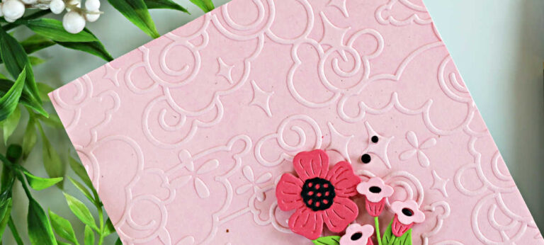 Handmade pink card featuring a soft blush ink-blended background embossed with the Spellbinders January 2026 Embossing Club “Cloud Nine” folder, layered die-cut flowers from the Small Die of the Month, and a black heat-embossed “Have a Nice Day” sentiment from the Clear Stamp and Die of the Month, finished with black gems.