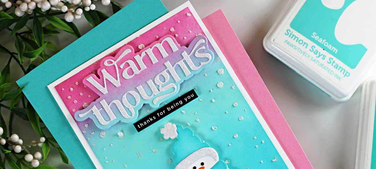 Handmade winter card featuring a bundled snowman die cut wearing a teal hat and scarf on a pink, purple, and teal ink-blended background. The card includes a layered “Warm Thoughts” sentiment at the top, a small “thanks for being you” label, and glitzy falling snow accents scattered across the background.