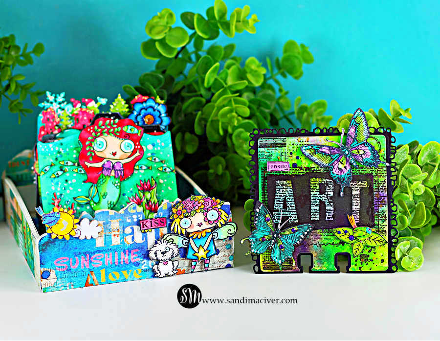 Colorful mixed media display featuring a vibrant AALL & Create MemoryDex card on the right and a decorated storage box on the left. The MemoryDex card has a neon green and purple Distress Oxide spray background with bold black “ART” lettering, hand-colored butterflies in teal and purple, and a small green bird with purple rhinestone accents. Beside it, a whimsical teal box is filled with bright florals and features a red-haired mermaid illustration, playful characters, and layered collage elements. The scene is styled with lush green foliage against a teal backdrop.