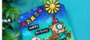 Colorful MemoryDex birthday card featuring a blue-to-teal ink blended background with splatter detail, festive banner flags, and a smiling sun. A cute girl in a party hat holds a birthday cake with candles beside a fluffy white dog, surrounded by bright flowers and green grass. The sentiment “Happy Birthday” appears on black labels in the center.