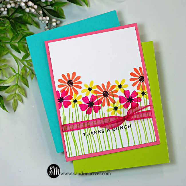 One-layer handmade thank-you card featuring colorful stamped wildflowers from the My Monthly Hero Wildflower Stamp and Cut set. Pink, coral, and yellow flowers with black centers rise from simple green stems on a white background, accented with a bright pink ribbon bow across the lower third and a stamped “Thanks a Bunch” sentiment.