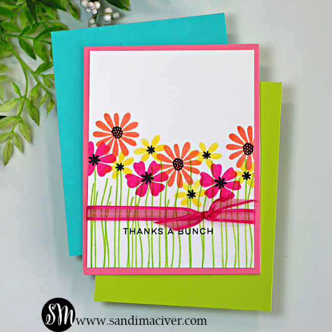 One-layer handmade thank-you card featuring colorful stamped wildflowers from the My Monthly Hero Wildflower Stamp and Cut set. Pink, coral, and yellow flowers with black centers rise from simple green stems on a white background, accented with a bright pink ribbon bow across the lower third and a stamped “Thanks a Bunch” sentiment.