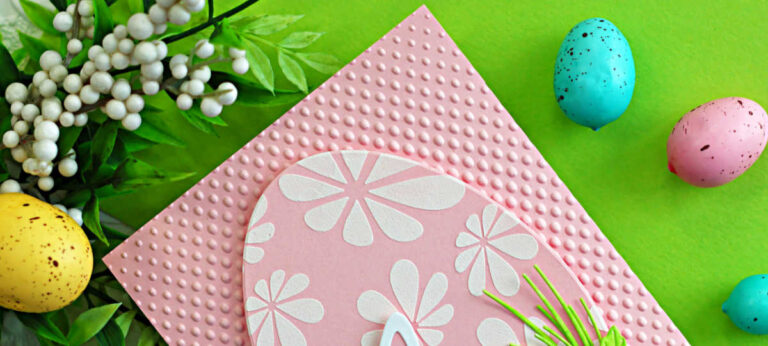 Handmade pink Easter card featuring a white Flourish Rabbit die cut layered over a Retro Daisies stenciled egg background, accented with layered spring flowers and greenery on an embossed pink panel.