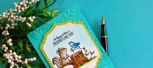 Handmade card featuring a Copic colored squirrel and blue bird sitting on a tree stump with the sentiment “So happy to have a friend like you,” layered on a teal embossed leaf background using an embossing folder and framed with a decorative die cut.