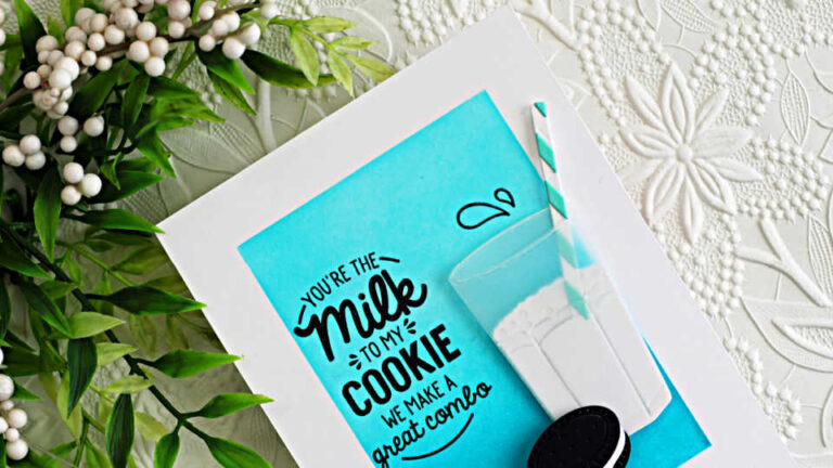A handmade card featuring a white A2 card base with a bright turquoise ink-blended panel in the center. A bold black sentiment reads, “You’re the Milk to My Cookie — We Make a Great Combo.” To the right is a dimensional die-cut glass of milk with a striped straw, and along the bottom are three Oreo-style sandwich cookies. The card is photographed on a white embossed floral background with greenery in the upper corner and color swatches partially visible to the side.