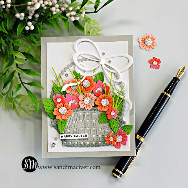 Handmade Easter card featuring the Country Basket Bouquet Die and Double Loop Bow from the Simon Says Stamp Beautiful Moments release. A textured die-cut basket filled with coral, peach, and pink flowers with layered green leaves sits on a white panel layered over a Fog cardstock card base. A large white double loop bow tops the basket, while small gems add sparkle and a “Happy Easter” sentiment completes the cheerful spring design.