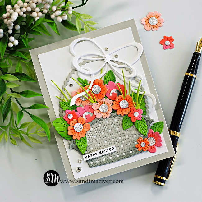 Handmade Easter card featuring the Country Basket Bouquet Die and Double Loop Bow from the Simon Says Stamp Beautiful Moments release. A textured die-cut basket filled with coral, peach, and pink flowers with layered green leaves sits on a white panel layered over a Fog cardstock card base. A large white double loop bow tops the basket, while small gems add sparkle and a “Happy Easter” sentiment completes the cheerful spring design.