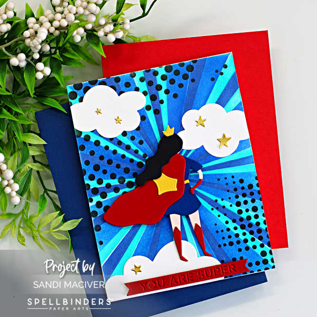 Handmade superhero-themed greeting card featuring a stylized Wonder Woman–inspired die-cut figure with a red cape and blue outfit standing against a vibrant blue burst background created with layered stencils. The background radiates with teal and navy rays and black halftone dots, with white clouds and small gold stars scattered around. A red banner at the bottom reads “YOU ARE SUPER.” Card created with the Spellbinders Small Die of the Month Unstoppable and the Burst Mode Layering Stencil of the Month.