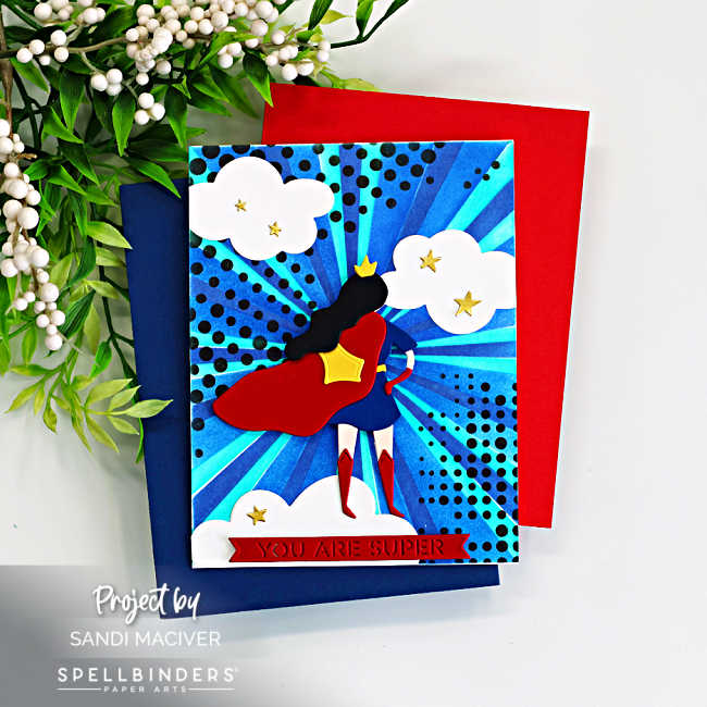 Handmade superhero-themed greeting card featuring a stylized Wonder Woman–inspired die-cut figure with a red cape and blue outfit standing against a vibrant blue burst background created with layered stencils. The background radiates with teal and navy rays and black halftone dots, with white clouds and small gold stars scattered around. A red banner at the bottom reads “YOU ARE SUPER.” Card created with the Spellbinders Small Die of the Month Unstoppable and the Burst Mode Layering Stencil of the Month.