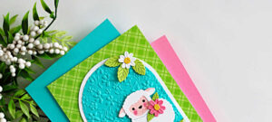 Handmade Easter lamb card created with the Simon Says Stamp Sweet Sheep die and A2 Arches dies, featuring a white sheep holding a flower on an embossed turquoise arch background with daisies and green patterned paper.