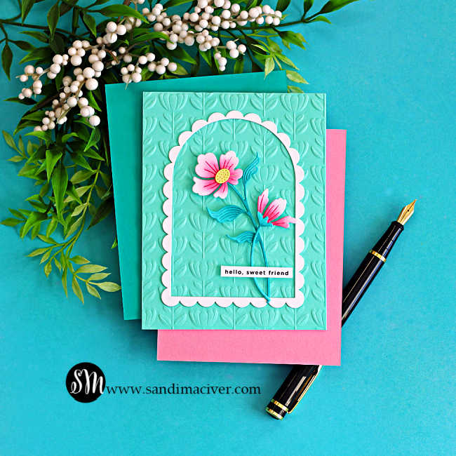 Elegant floral arch card with pink die cut flowers on an aqua embossed background with scalloped frame, styled with greenery and a black fountain pen