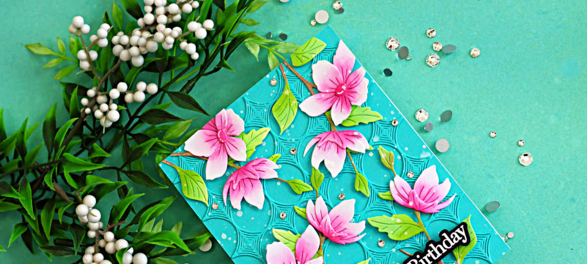 Elegant blossom branch die cut spring card featuring pink flowers, green leaves, and a teal embossed background with a Happy Birthday sentiment.