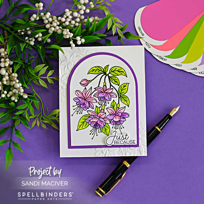 White space card featuring pink and purple fuchsia flowers inside an arched frame on a white embossed background, styled on a purple surface with greenery and a fountain pen.
