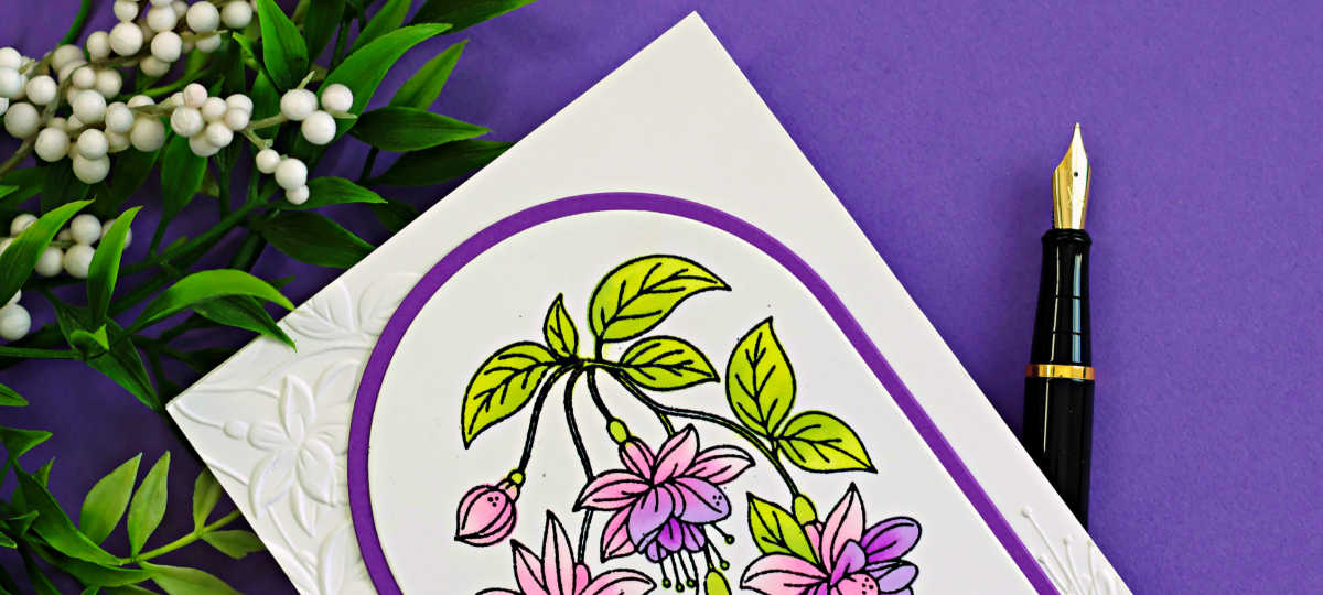 Clean floral fuchsia card featuring pink and purple flowers in an arched frame on a white embossed background, styled with greenery and a purple backdrop.