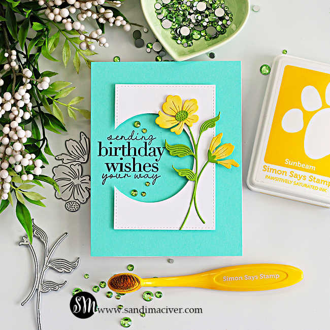 Floral birthday card featuring a circle die cut design with “sending birthday wishes your way” sentiment, layered yellow flowers, teal card base, and green embellishments, surrounded by cardmaking supplies
