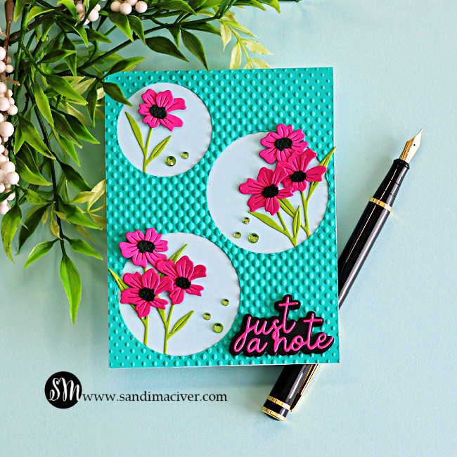 Handmade die cut floral card featuring bright pink flowers inside stitched circle frames on a teal halftone embossed background with a “just a note” sentiment.