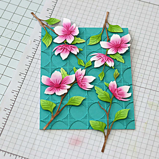 Arranging die cut blossom branches and flowers on embossed background for a die cut spring card.