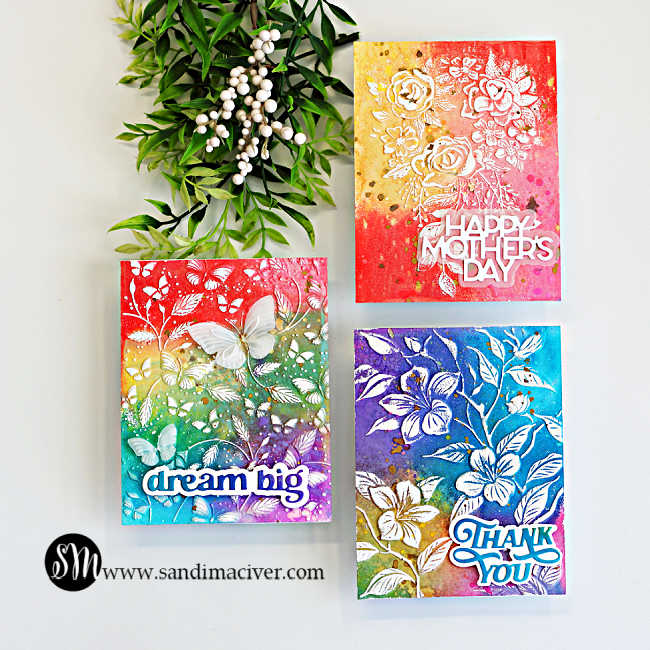 Three colorful handmade cards created with an embossing folder technique for cardmaking, featuring Distress Oxide ink blended backgrounds and white heat embossed floral designs with “Happy Mother’s Day,” “Dream Big,” and “Thank You” sentiments.