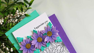 Easy floral die cut card featuring purple layered flowers and teal leaves on a clean white background, demonstrating how to embrace white space in cardmaking with a stamped gerbera daisy background and simple sentiment.