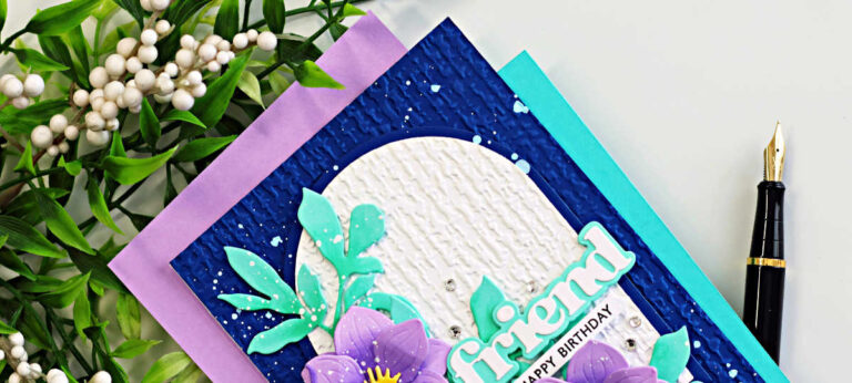 Delicate magnolia die cut card with purple layered flowers, teal leaves, and embossed organic linen arch on a navy background with splatter details and “friend” birthday sentiment