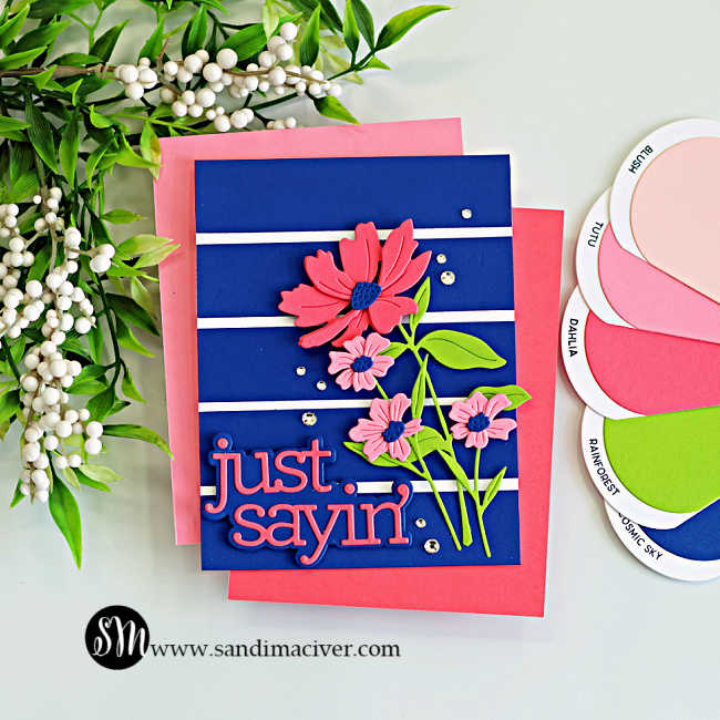 Bold navy background die cut floral card featuring pink layered flowers with blue centers, bright green leaves, white stripe accents, and a large “just sayin’” sentiment for a dramatic cardmaking color combo.