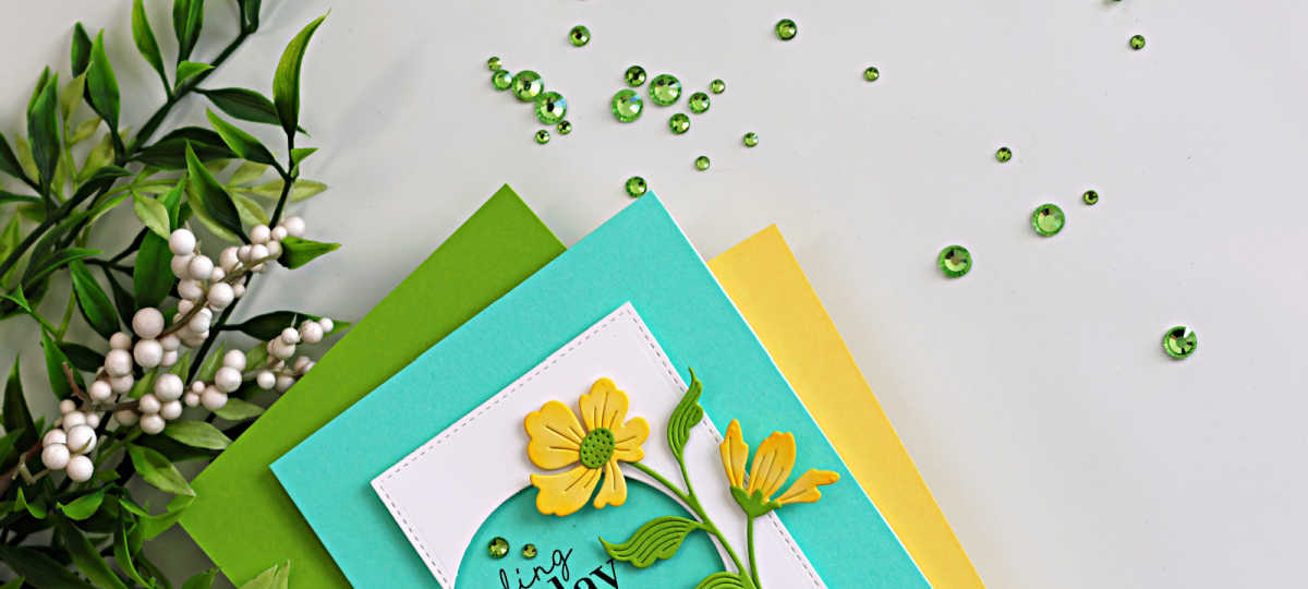 Floral die cut birthday card featuring a circle cut from the front panel, with teal, yellow, and green cardstock layers and scattered green gems, showcasing a simple cardmaking technique that adds depth and interest