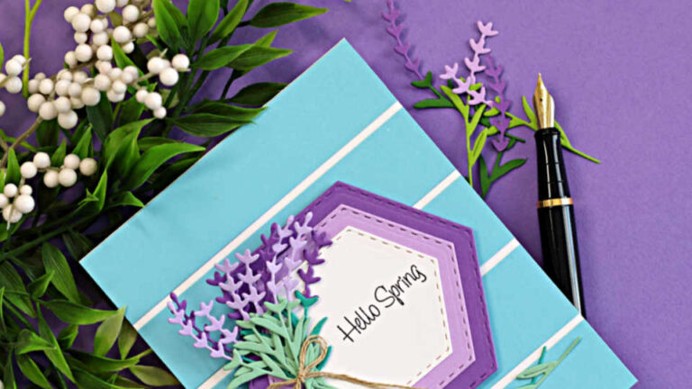 Simple die cut lavender card with layered hexagon frames, striped background, and delicate lavender sprigs on a purple surface with greenery and a pen