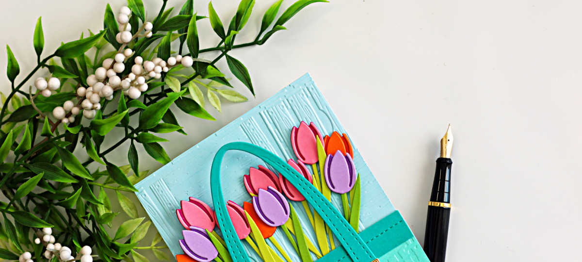 Spring tulip market tote card made with Spellbinders Large Die of the Month, featuring colorful die cut tulips, embossed background, and layered paper crafting details.