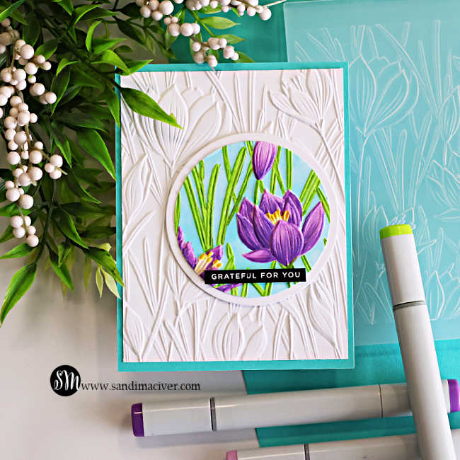 Handmade spotlight technique card featuring the Simon Says Stamp Crocus Field embossing folder with a circular crocus flower focal point colored in purple and green with Copic markers on a white embossed background and aqua card base.