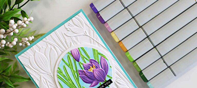 Handmade spotlight technique card featuring the Simon Says Stamp Crocus Field embossing folder with a circular crocus floral focal point colored using purple and green Copic markers on a white embossed background with aqua card base.