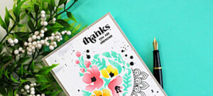 Close-up of a clean and simple floral thank you card featuring soft ink-blended pink and yellow flowers with mint green leaves from the Altenew Dynamic Duo Crescent Flowers stamp and stencil set. The modern card design includes black splatter details, bold sentiment stamping, and an outline arch accent on a white background.