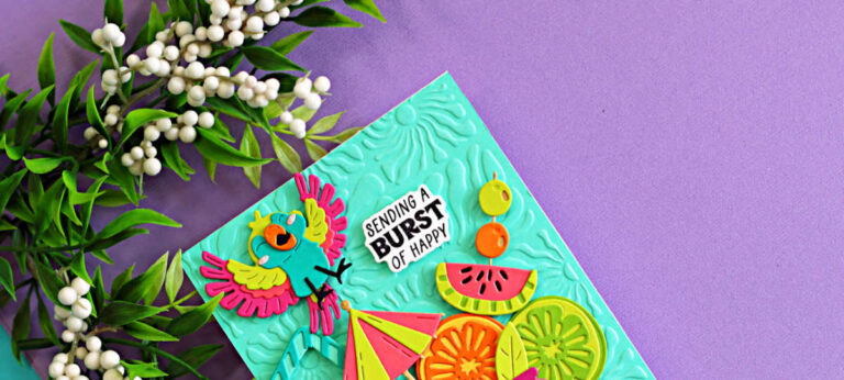 Colorful tropical die cut card featuring a bright parrot, citrus slices, watermelon, and umbrella created with the Spellbinders May Large Die of the Month. The aqua embossed background from the Radiant Day 3D Embossing Folder adds sunny texture to this Caribbean color splash summer card design.